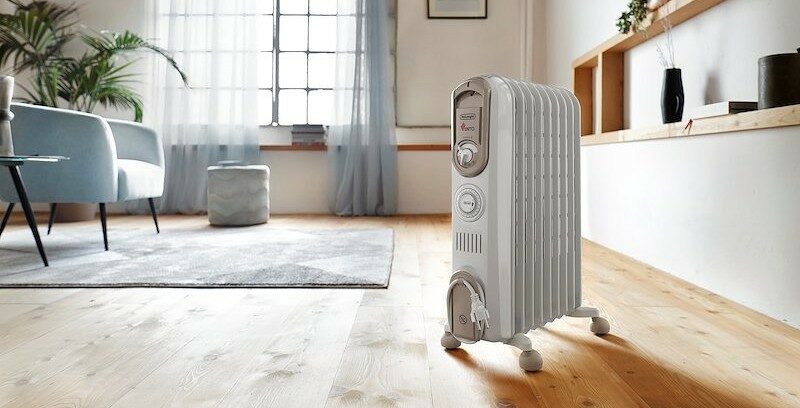 Un radiatore elettrico bianco è posizionato nel soggiorno di una casa, sopra al pavimento in legno